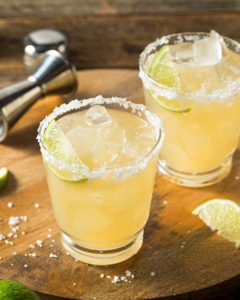2 margarita cocktails in rocks glasses sit on a brown table, made by the best classic margarita recipe
