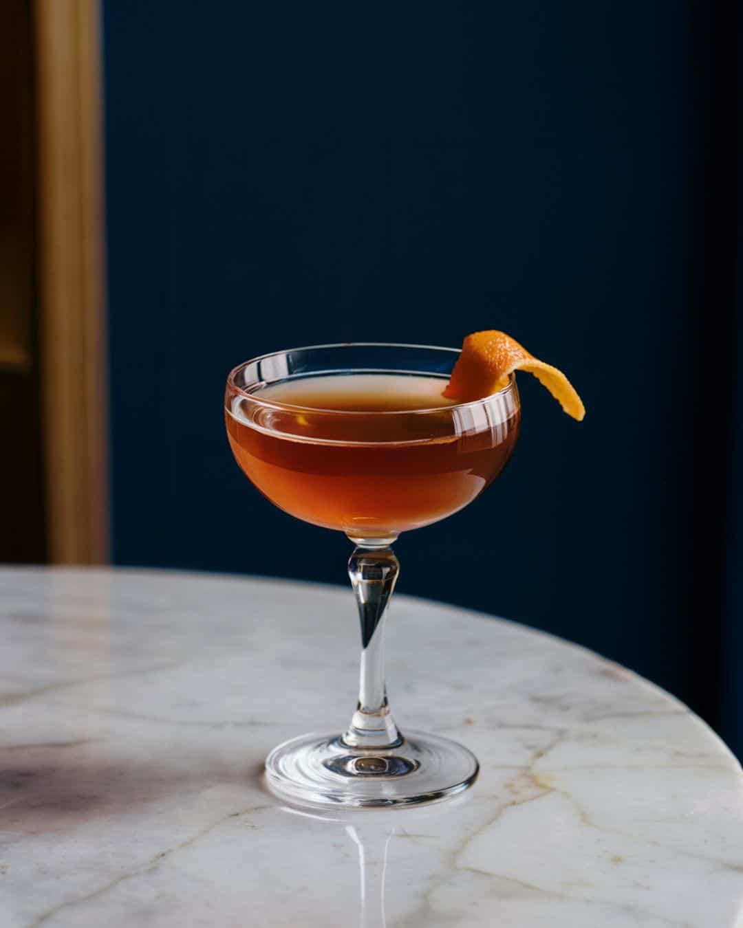 tequila old fashioned cocktail on a marble table garnished with an orange twist
