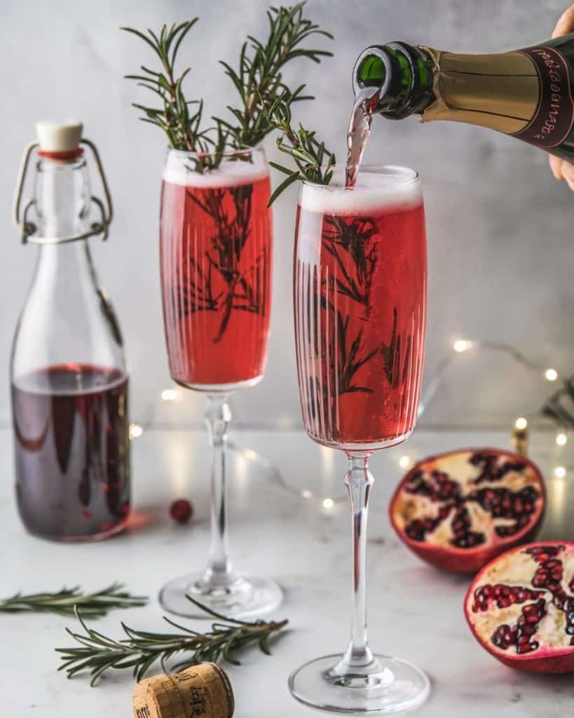pomegranate champagne cocktail on a marble table next to juice and seeds for a christmas party