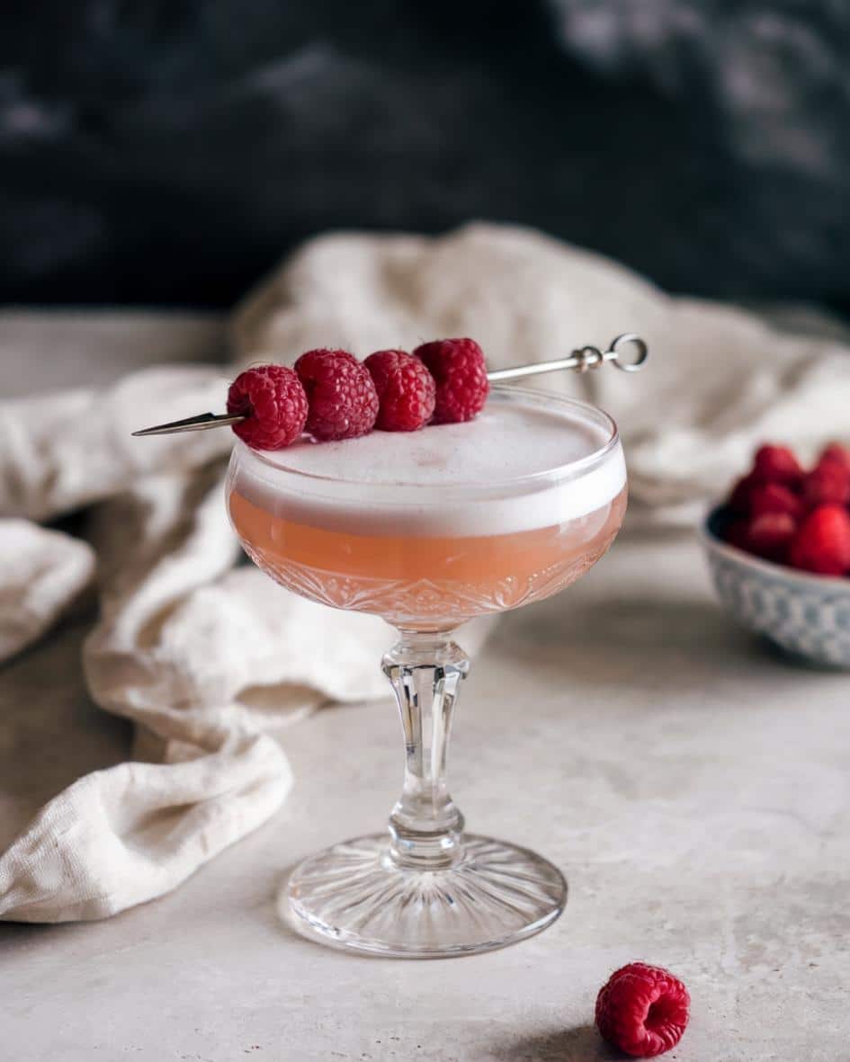 A classic clover club recipe featuring a gin-based cocktail with tart raspberry flavor, creamy foam, and a raspberry garnish.